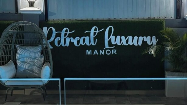Une piscine avec un bord carrelé, un fauteuil de relaxation et un panneau indiquant : « Retreat Luxury Manor ».