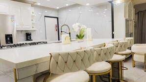 Une cuisine moderne avec un plan de travail en marbre, une cuisinière à gaz, des tabourets de bar blancs et une plante décorative.