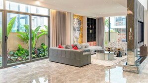 A modern living room with a grey sofa, red cushions, a zebra-patterned chair, and a large TV. - Regal Riverside Villas (Da Nang)