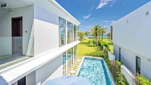 A modern hotel with a pool, a balcony, and a view of the lawn and palm trees. - Regal Riverside Villas (Da Nang)