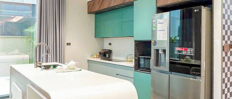 Una cocina moderna con una isla integrada, electrodomésticos de acero inoxidable, armarios color turquesa y un amplio ventanal.