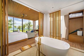 Una habitación de hotel moderna con una cama grande, una bañera, un sofá y vistas a palmeras.