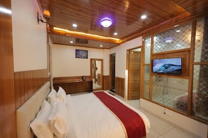 A hotel room with a wooden ceiling, a large bed with white and red bedding, a television on the wall, and a mirror.
