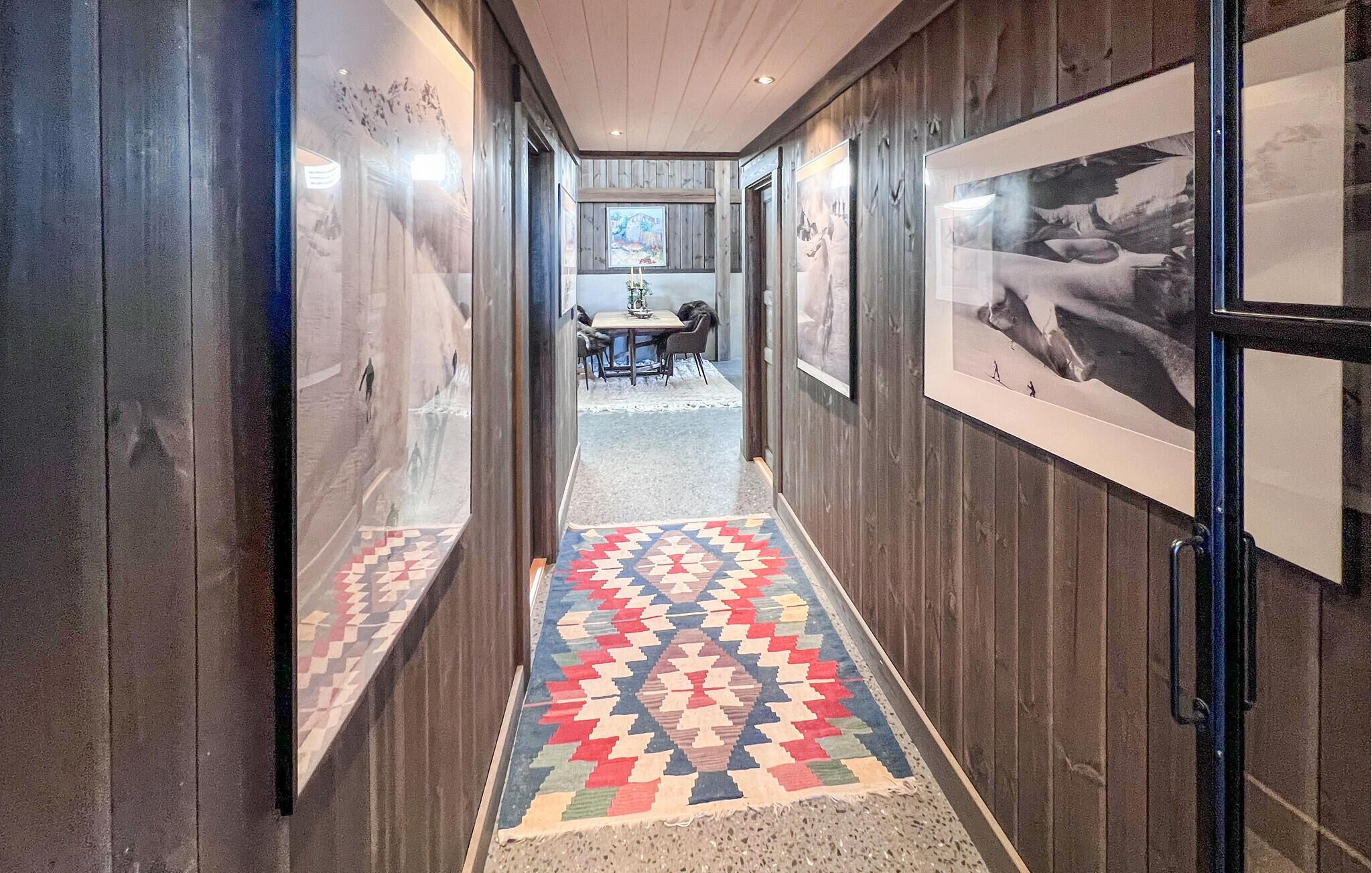 A hallway with wooden walls, a patterned rug, and framed pictures on the walls.