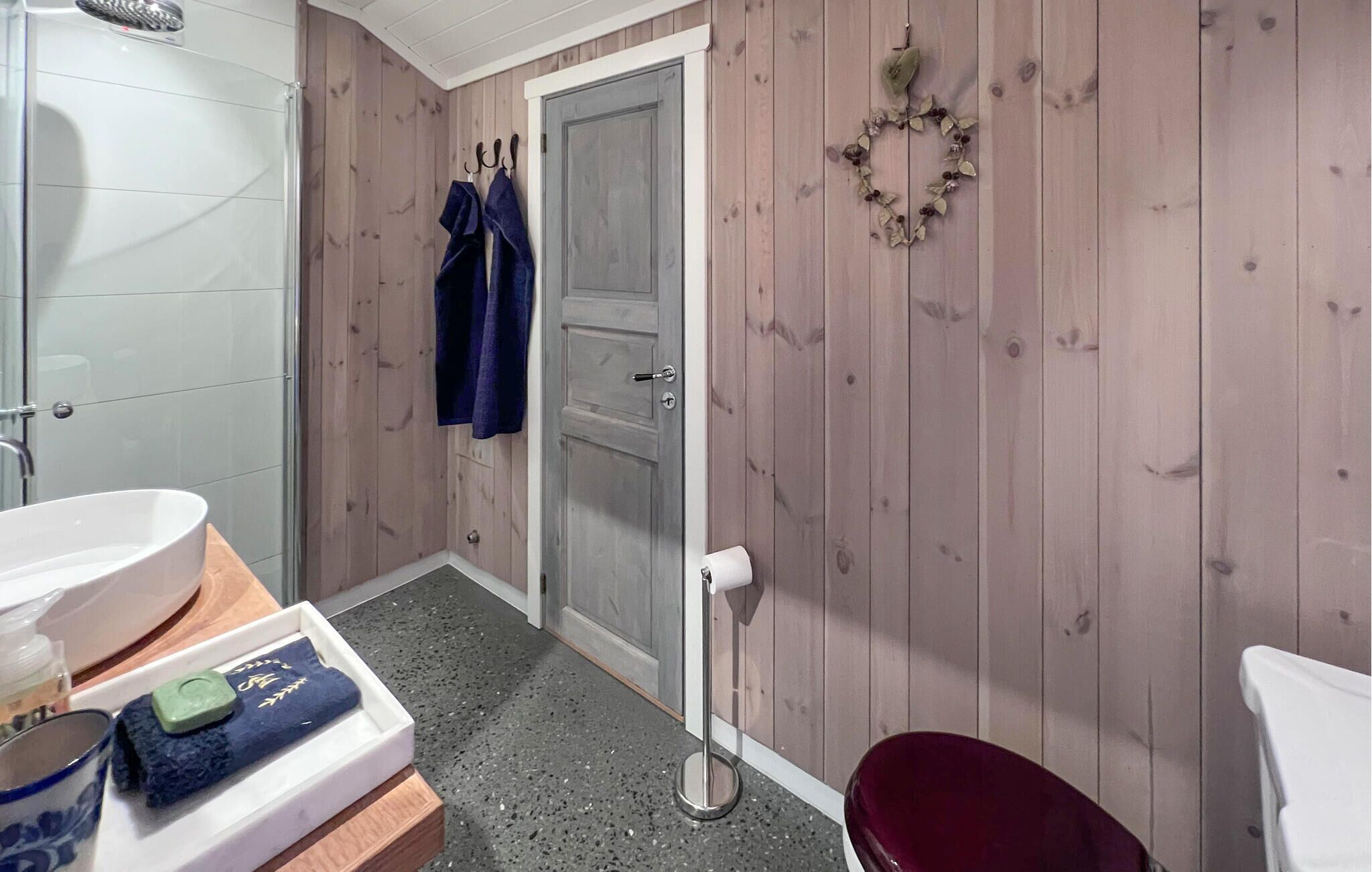 A bathroom with a white sink, a wooden door, a towel rack with towels, a toilet, and a small decorative wreath.