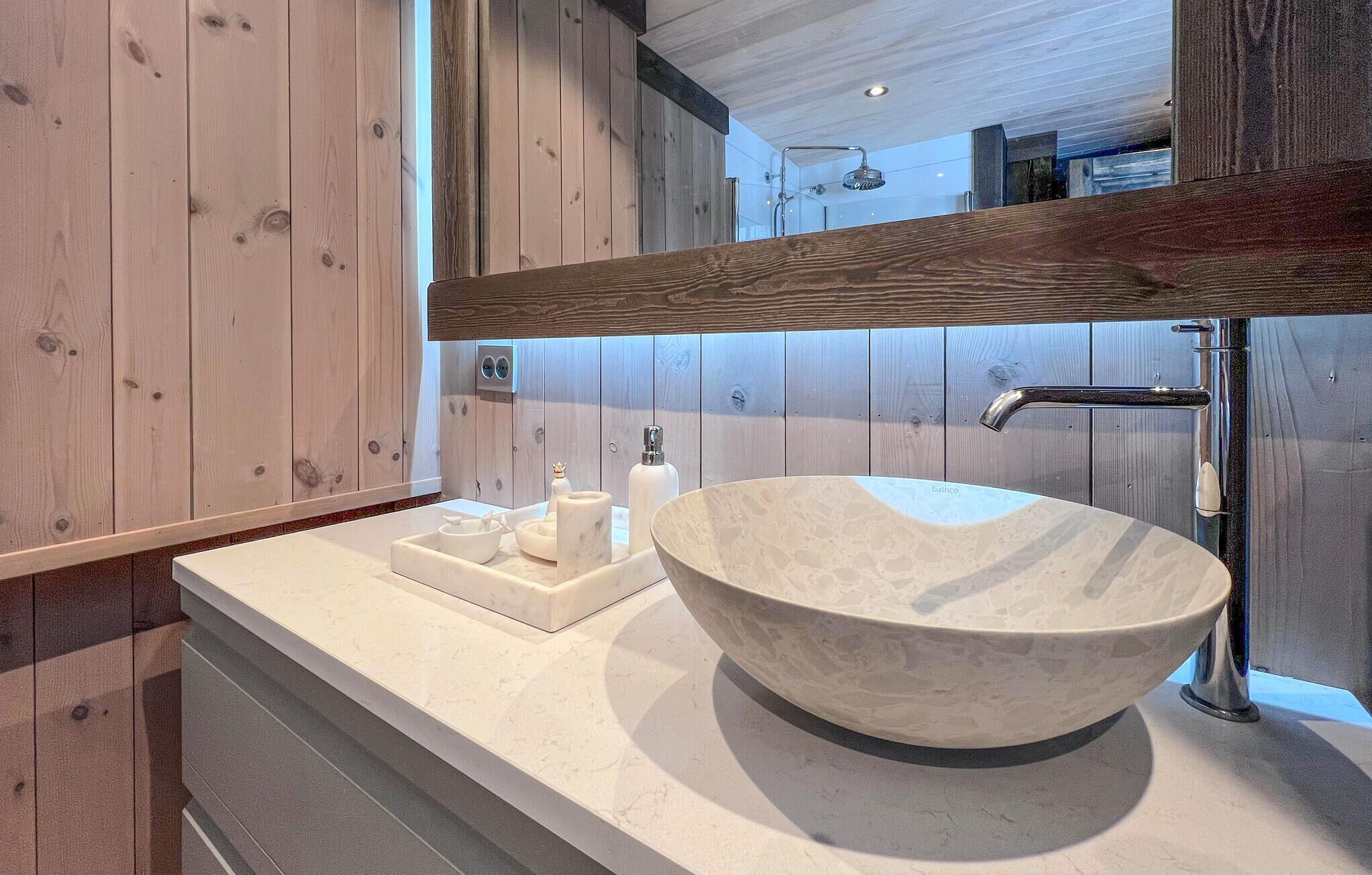 A modern bathroom with a large, round, textured sink, a wooden vanity, and a mirror above the sink.