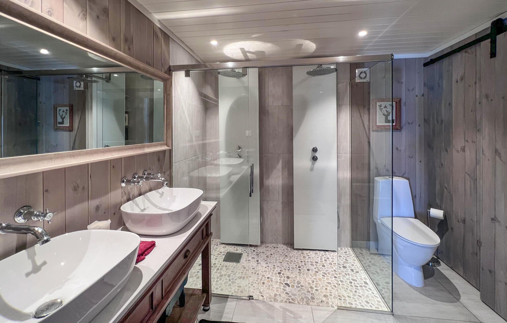 A bathroom with a wooden wall, a glass shower enclosure, a white sink, and a toilet.