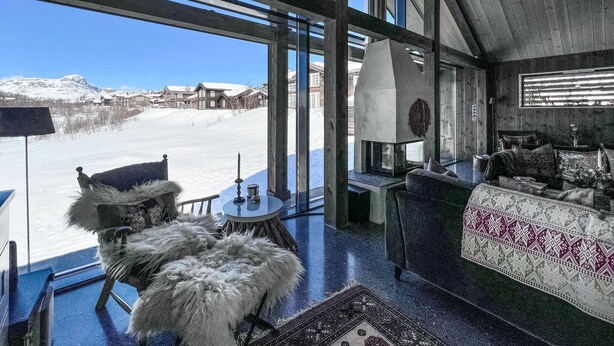 Ein Zimmer mit hohen Decken, einem großen Fenster mit Blick auf eine verschneite Landschaft, einem Kamin und einer gemütlichen Sitzecke.