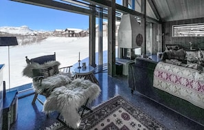 A high-ceilinged room with a large window overlooking a snowy landscape, a fireplace, and a cozy seating area.
