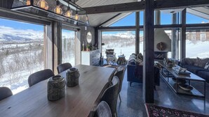 Ein geräumiger Raum mit einem großen Holztisch, Stühlen, einer Couch und Blick auf eine verschneite Landschaft durch große Fenster.