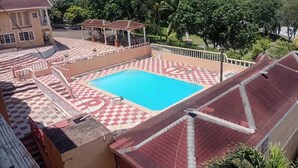 Une piscine entourée d’un motif à carreaux, un espace de repos couvert et une vue sur la verdure environnante.