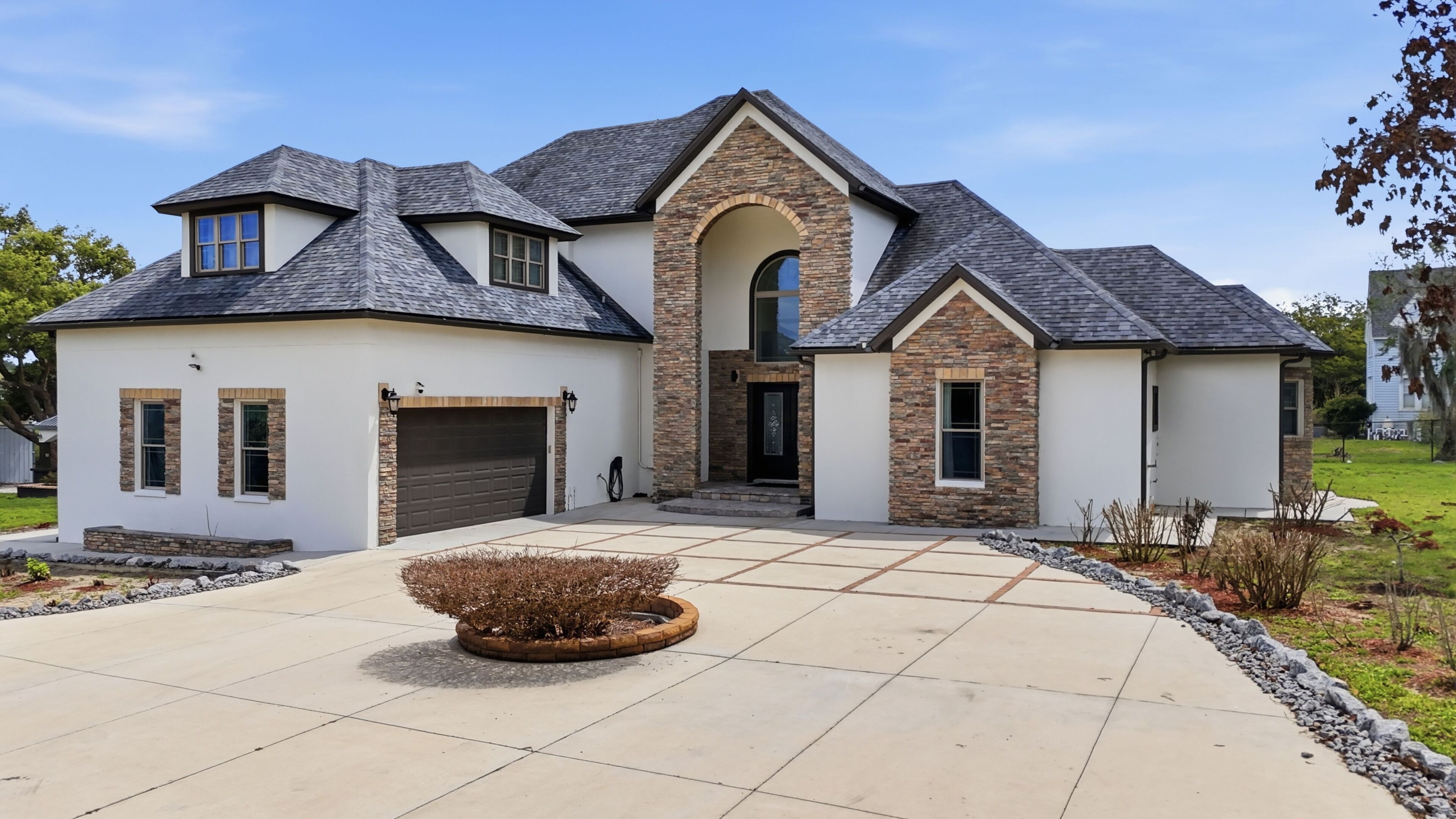 A modern two-story house with a stone facade, a garage, and a landscaped driveway.