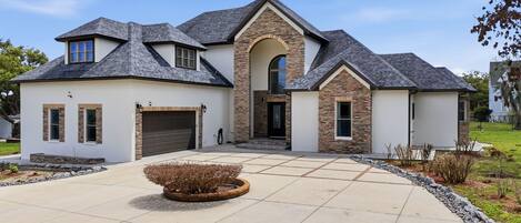 A modern two-story house with a stone facade, a garage, and a landscaped driveway.