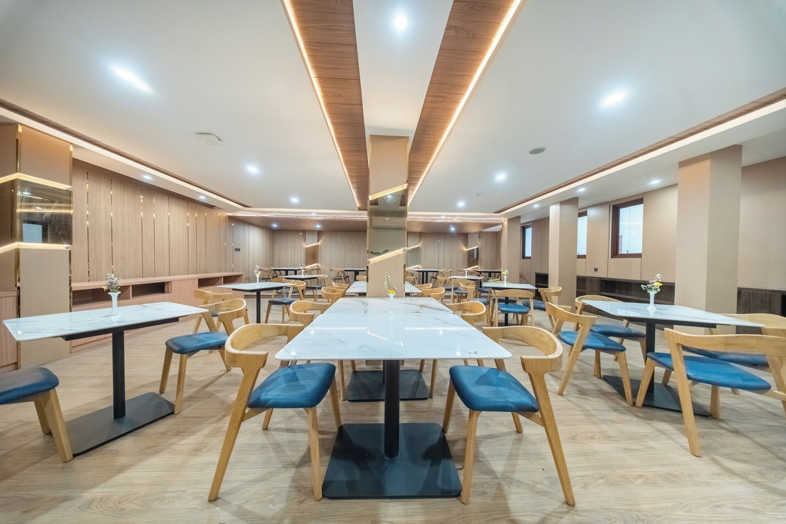 Un amplio comedor con varias mesas y sillas, piso de madera y un diseño de techo moderno.