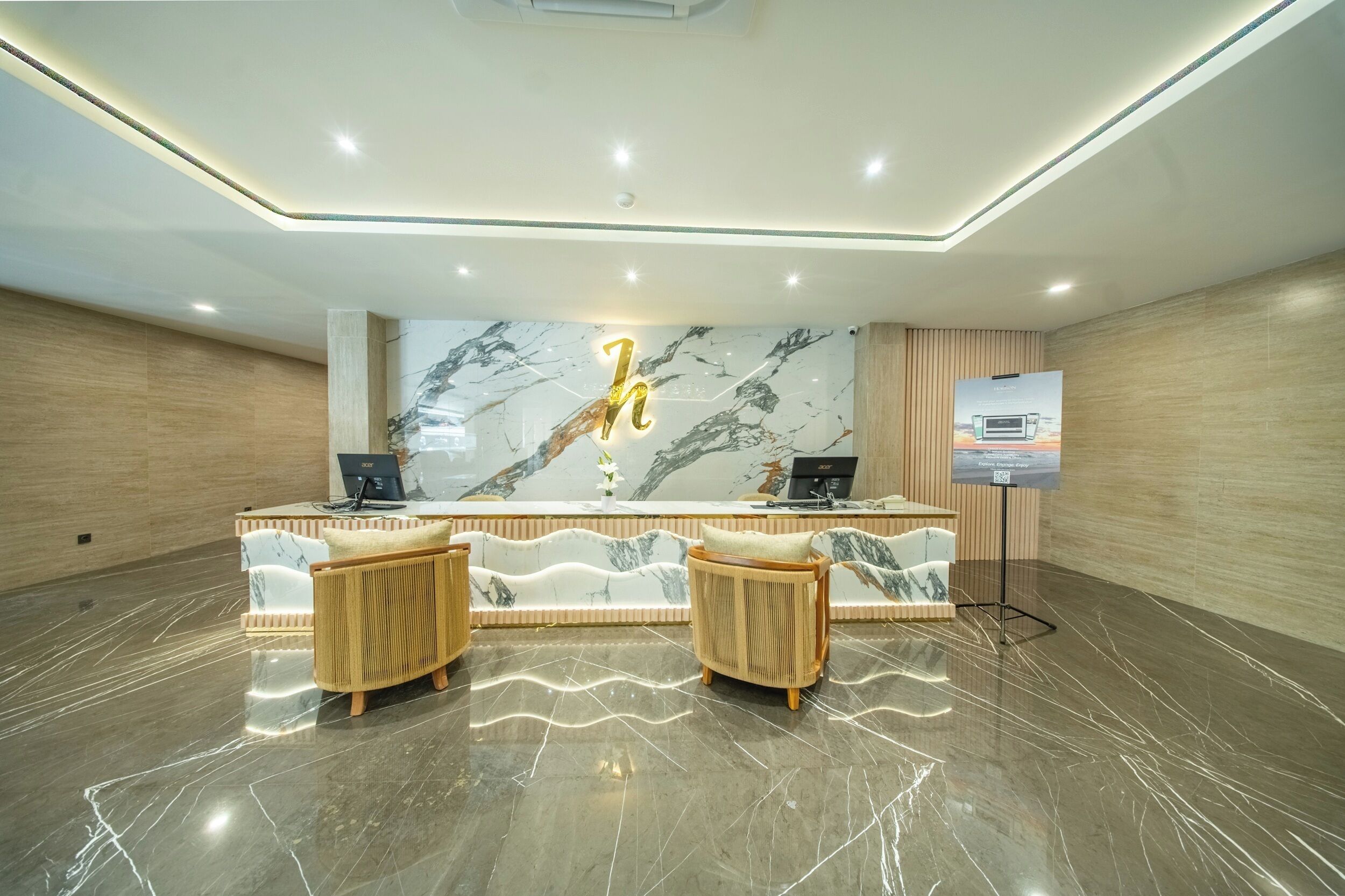 A reception area with a marble wall, two cushioned chairs, a desk with a computer, and a poster on the wall.
