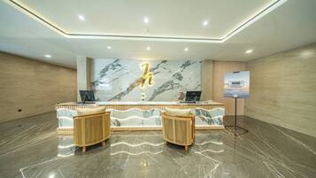 A reception area with a marble wall, two cushioned chairs, a desk with a computer, and a poster on the wall.