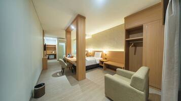 A hotel room with a bed, a desk, a chair, a wardrobe, and a small trash bin.