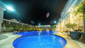 A nighttime swimming pool with a circular shape, surrounded by a landscaped area with plants and a building with classical architectural details. - Horison IJ Kudus (Kudus)
