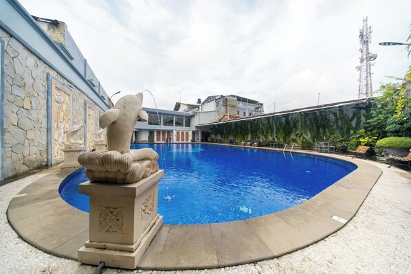 A swimming pool with a stone sculpture, a stone wall, and a building with a modern design in the background. - Horison IJ Kudus (Kudus)