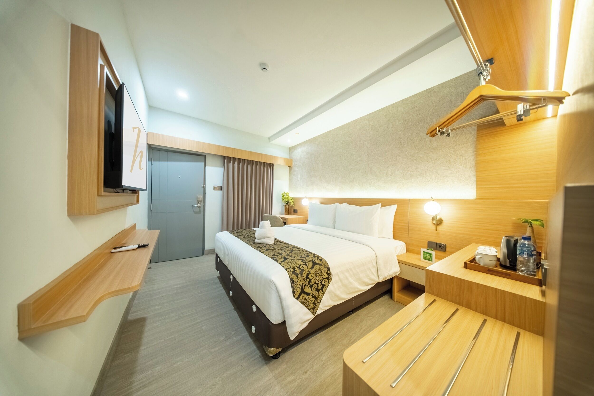 A hotel room with a bed, bedside table, TV, wooden wall, and a mirror.