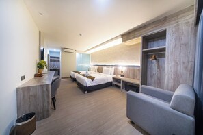 A modern hotel room with a wooden desk, two beds, a sofa, a small table, and a mirror. - Horison IJ Kudus (Kudus)