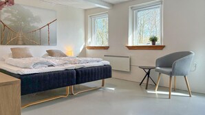 Un dormitorio con cama, mesita de noche, silla, ventanas y un radiador.