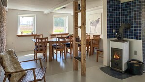 Un comedor con sillas de madera y una mesa, una chimenea con revestimiento de azulejos y ventanas con vistas al verdor.
