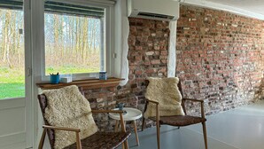 Una habitación con pared de ladrillo, dos sillas, una mesita y una ventana que da a las árboles.