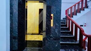 Un ascenseur moderne au design géométrique, un escalier rouge avec des rampes en bois et un sol en marbre.