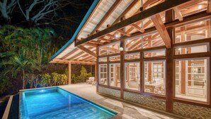 A poolside area with a clear pool, wooden pergola, and a view into a room with a dining area. - Villa 4 - The Ledge - Infinity Pool Overlooking the Ocean & Mountains (Chinampas)
