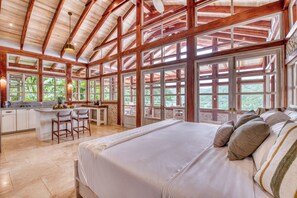 A spacious room with a large bed, a kitchen area, and a dining space with a view of greenery. - The Ledge - Infinity Pool Overlooking the Ocean & Mountains (Chinampas)