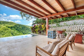A covered outdoor area with a pool, wooden furniture, and a stone wall. - The Ledge - Infinity Pool Overlooking the Ocean & Mountains (Chinampas)