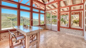 A spacious room with large windows, a stone wall, and a wooden ceiling. - Villa 4 - The Ledge - Infinity Pool Overlooking the Ocean & Mountains (Chinampas)