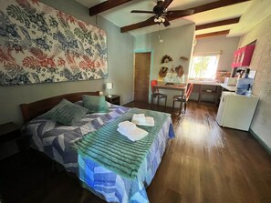 A bedroom with a bed, a desk, a chair, and a kitchenette.