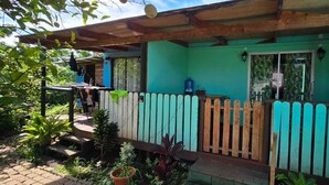 Una casa con porche de madera, una puerta azul y un tanque de gas afuera.