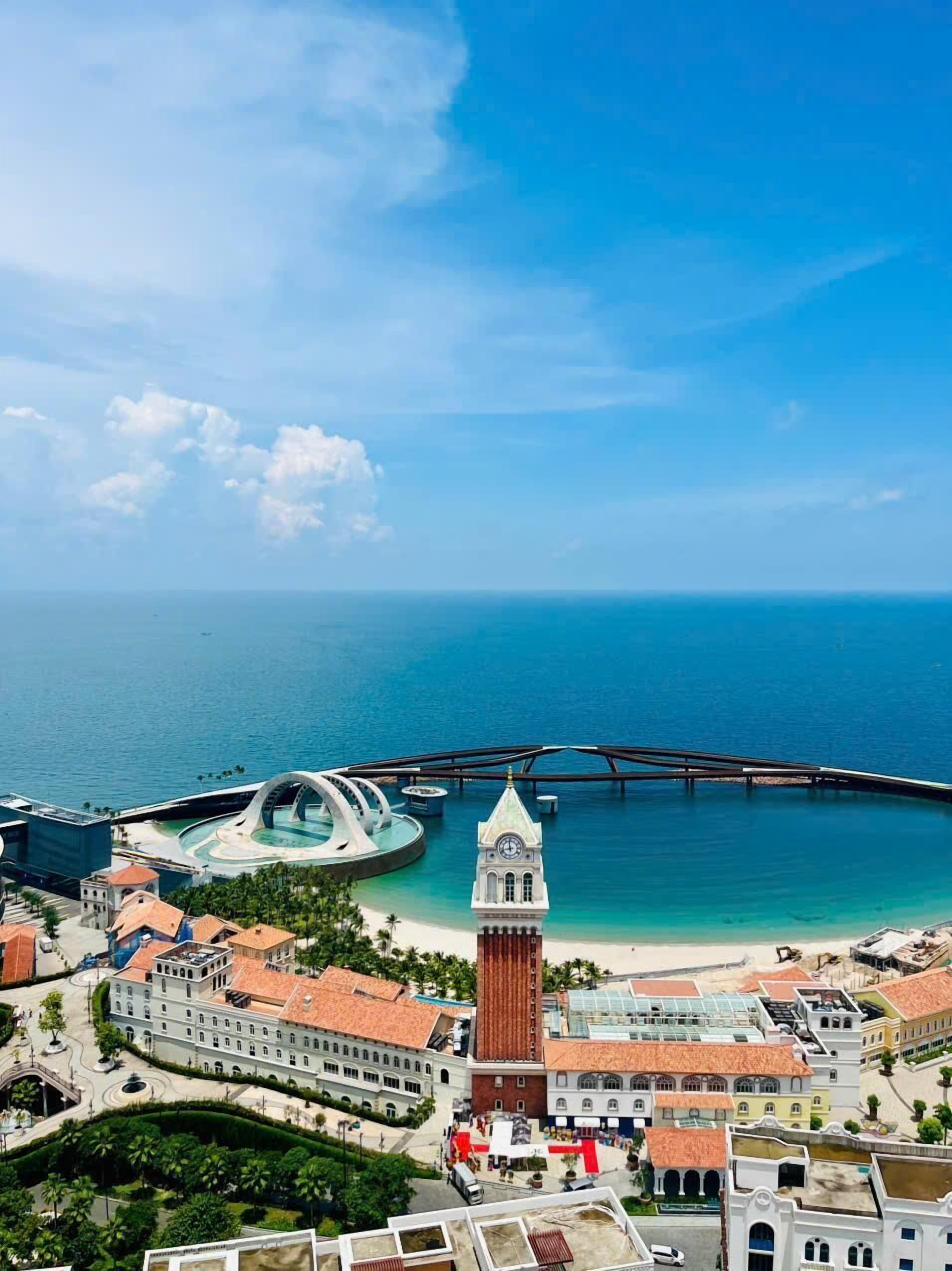 A coastal town with a prominent clock tower, a modern bridge, and a central plaza with buildings.