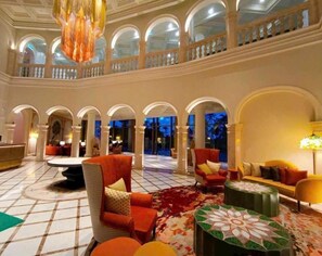 En rummelig lobby med hvælvede søjler, et højtloftet rum og et centralt siddeområde med sofaer og et sofabord.