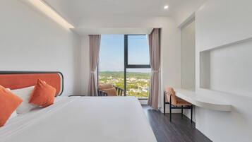 A hotel room with a large bed, a desk, and a view of a cityscape through a large window.