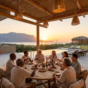 A group of people dining at an outdoor table with a view of the sunset over the water. - Nusa Retreat - Seaview luxury residences - ideal for groups (Kissamos)