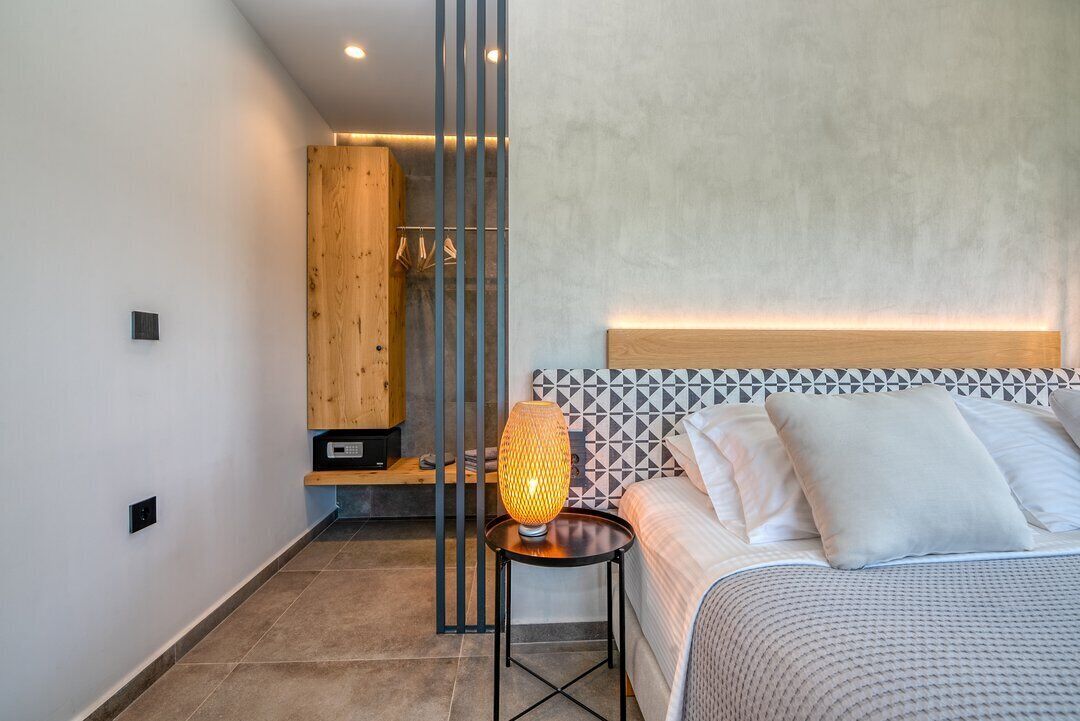 A modern bedroom with a bed, a bedside table with a lamp, a wooden wardrobe, and a geometric-patterned headboard.