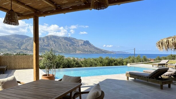 An outdoor pool area with lounge chairs, a wooden table, and a view of the sea and mountains. - Nusa Retreat - Seaview luxury residences - ideal for groups  (Kissamos)