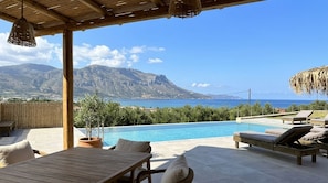 Un espace piscine extérieur avec des chaises longues, une table en bois et une vue sur la mer et les montagnes.