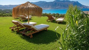 A grassy area with lounge chairs and a thatched structure, overlooking a body of water and mountains. - Nusa Retreat - Seaview luxury residences - ideal for groups  (Kissamos)