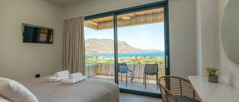 Habitación de hotel con cama, escritorio, silla, televisor y balcón con vista al mar.
