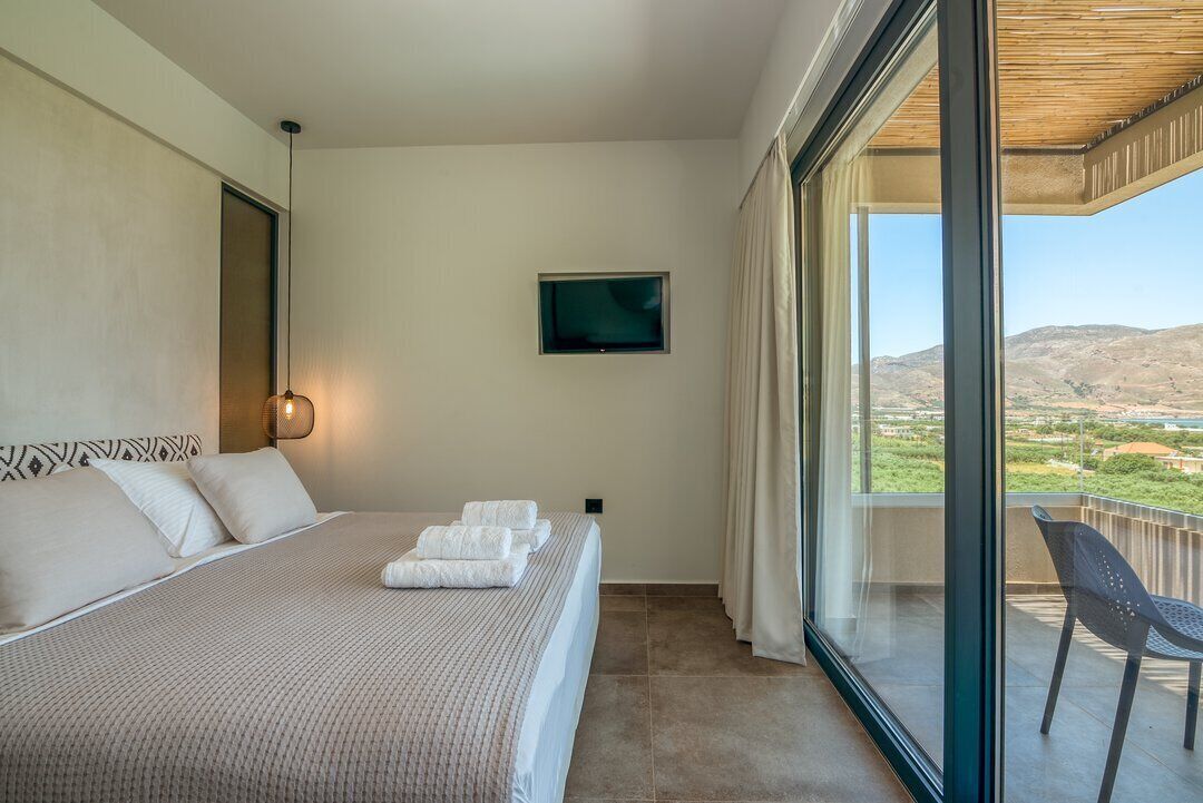 Une chambre d’hôtel avec un grand lit, un téléviseur fixé au mur et un balcon offrant une vue sur le paysage.