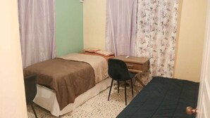 Ein kleines Schlafzimmer mit einem Einzelbett, einem Schreibtisch, einem Stuhl und zwei Vorhängen.