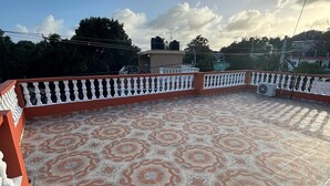 Eine Dachterrasse mit gemusterten Fliesen, einem weißen Geländer und einem Ventilator.