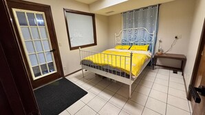 Ein Schlafzimmer mit einem Bett, einem kleinen Nachttisch, einem Fenster mit Vorhängen und einer Tür.