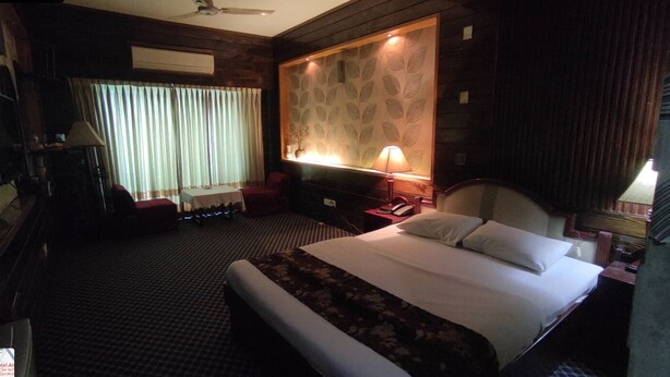 Habitación de hotel con una cama grande, un escritorio, una silla, una lámpara, un teléfono y una ventana con cortinas.