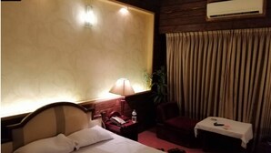 Una habitación de hotel con cama, lámpara de noche, silla, mesa y cortinas.